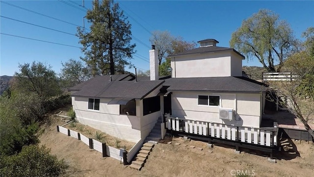 rear view of property featuring a shingled roof, a chimney, and stucco siding