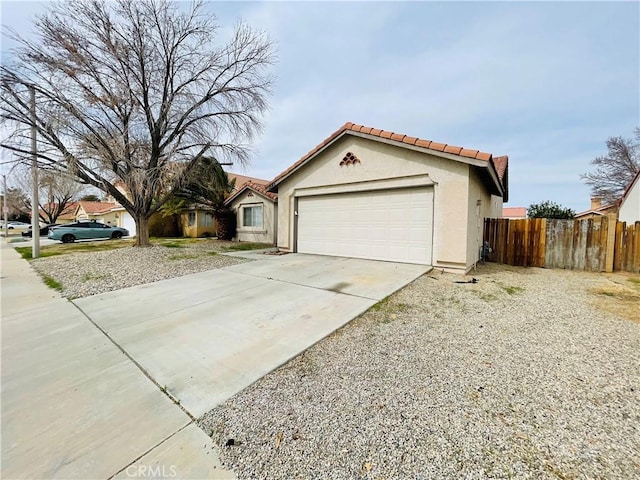 view of front of home featuring a tile roof, stucco siding, fence, a garage, and driveway