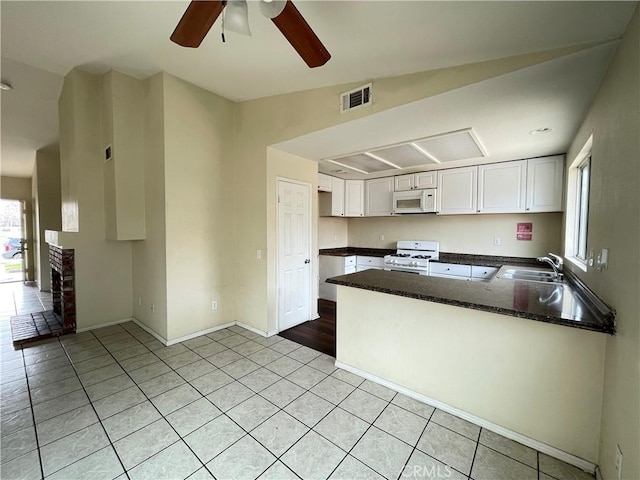 kitchen with white appliances, visible vents, white cabinets, a peninsula, and a sink