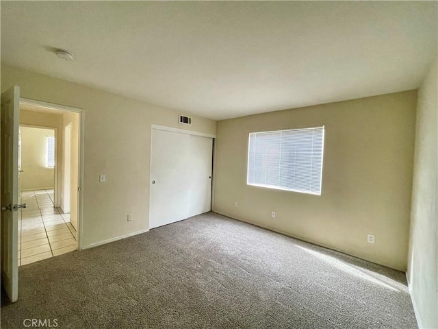 unfurnished bedroom featuring tile patterned flooring, a closet, visible vents, and carpet flooring