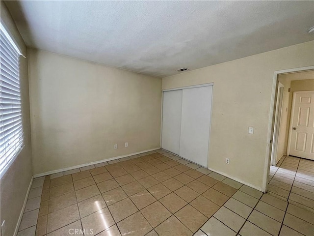 unfurnished bedroom with a closet, multiple windows, visible vents, and light tile patterned floors