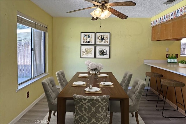 dining space featuring visible vents, a textured ceiling, baseboards, and wood finished floors