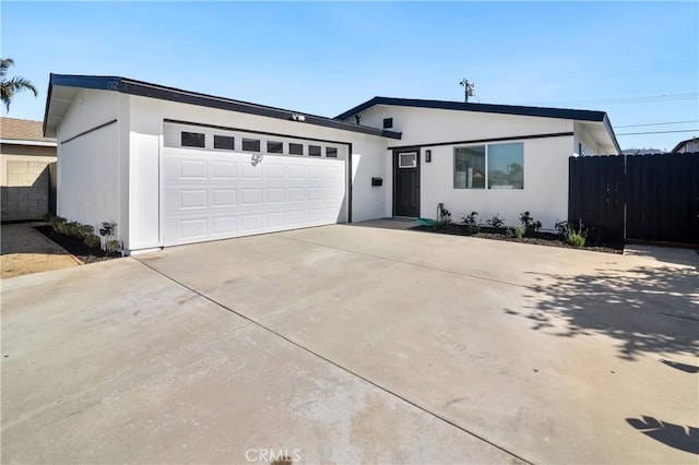 view of front of property featuring a garage, driveway, fence, and stucco siding