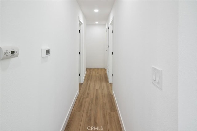 corridor featuring light wood-type flooring, baseboards, and recessed lighting