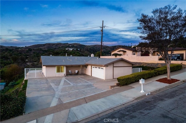 ranch-style home with concrete driveway, an attached garage, a gate, fence, and a mountain view