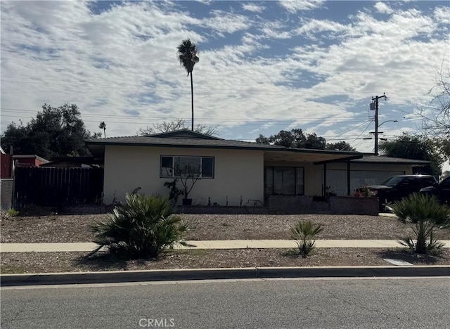 view of front facade with stucco siding, a garage, and fence