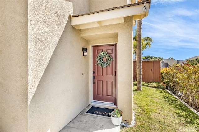 view of exterior entry with fence, a lawn, and stucco siding