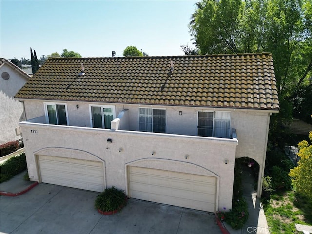 back of property featuring driveway, a tile roof, and stucco siding