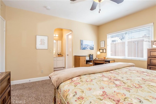 carpeted bedroom with a ceiling fan, arched walkways, ensuite bath, and baseboards