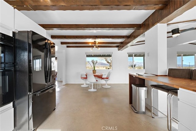 kitchen featuring black appliances, a healthy amount of sunlight, white cabinetry, and finished concrete floors