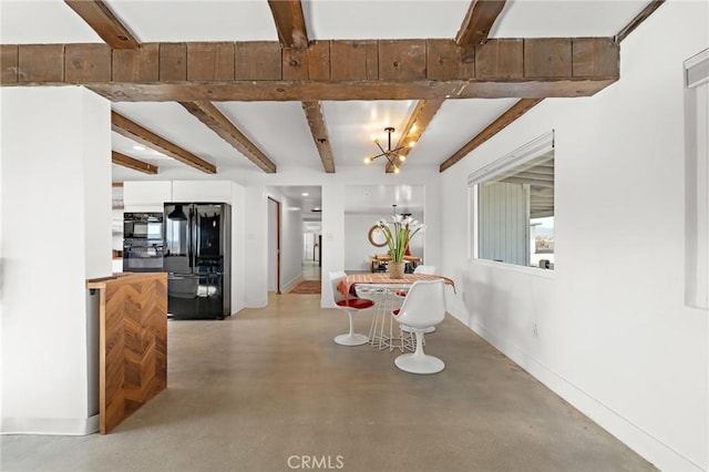 dining room featuring concrete flooring, a notable chandelier, beamed ceiling, and baseboards