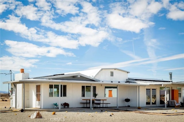 back of property featuring roof mounted solar panels and a patio