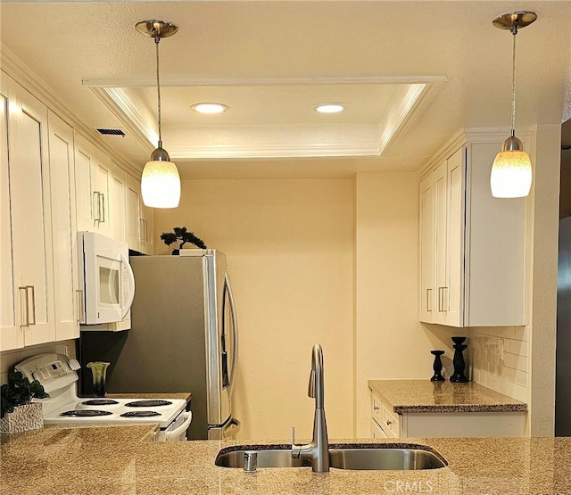 kitchen with light stone countertops, white appliances, a tray ceiling, and a sink