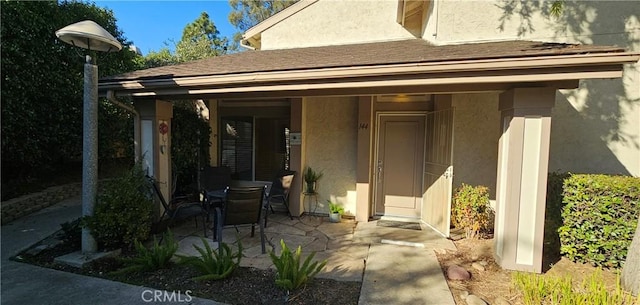 property entrance featuring a shingled roof, outdoor dining area, a patio area, and stucco siding