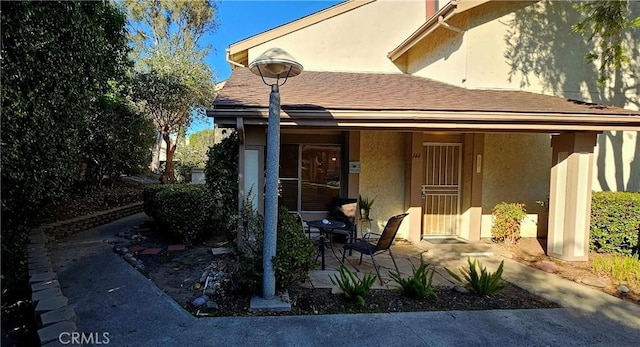 view of exterior entry featuring a patio area, roof with shingles, and stucco siding