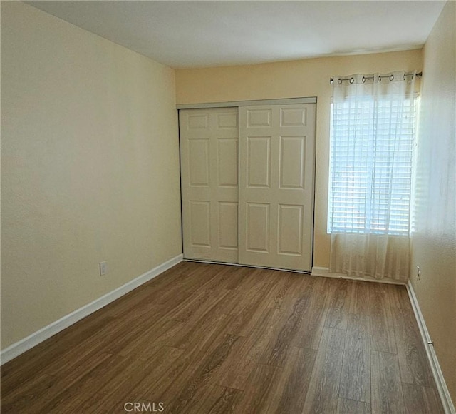 unfurnished bedroom with a closet, wood finished floors, and baseboards