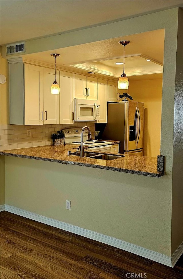 kitchen with a raised ceiling, visible vents, dark stone countertops, white appliances, and a peninsula