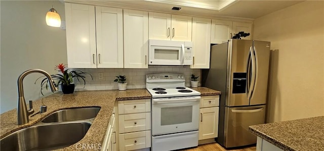 kitchen featuring white appliances, a sink, hanging light fixtures, backsplash, and dark stone counters