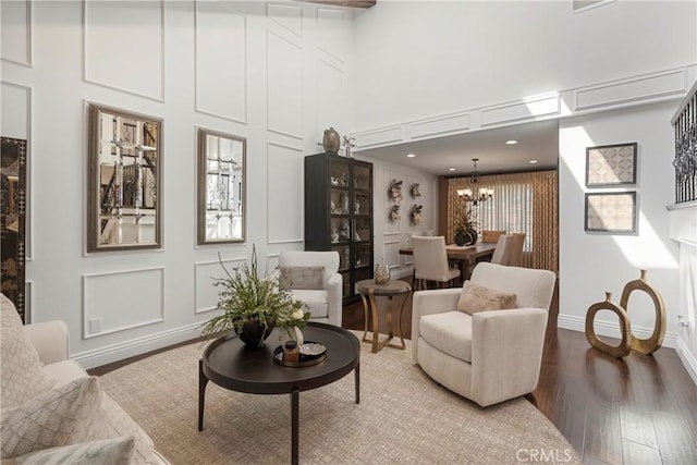 living area featuring a notable chandelier, a decorative wall, a high ceiling, wood finished floors, and baseboards