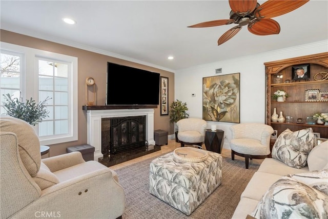 living area featuring ceiling fan, a glass covered fireplace, crown molding, and recessed lighting