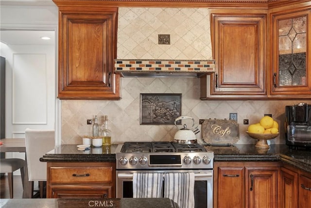 kitchen with tasteful backsplash, brown cabinetry, gas range, wall chimney exhaust hood, and glass insert cabinets