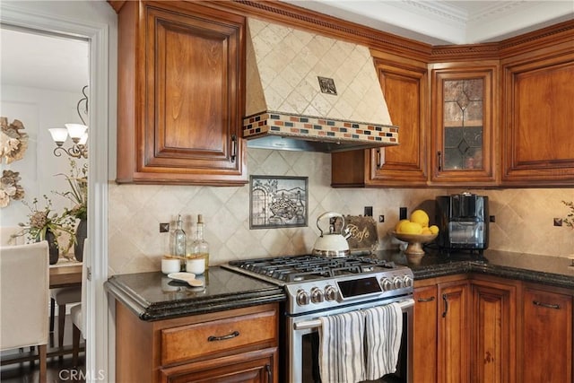 kitchen featuring brown cabinetry, wall chimney exhaust hood, glass insert cabinets, stainless steel range with gas stovetop, and backsplash