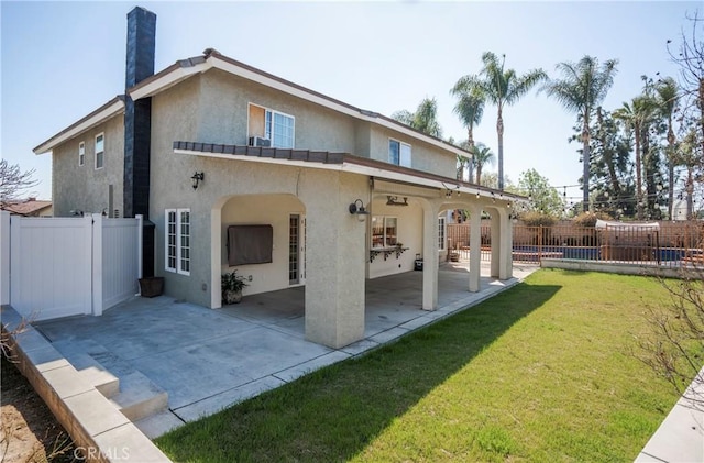 back of house featuring a lawn, a patio, a fenced backyard, a chimney, and stucco siding