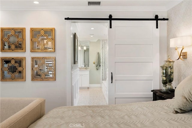 bedroom with visible vents, crown molding, ensuite bathroom, and a barn door