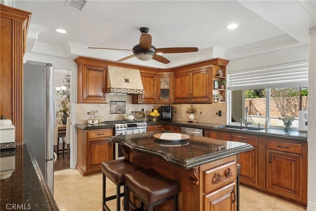 kitchen with stainless steel appliances, a sink, visible vents, wall chimney exhaust hood, and brown cabinetry