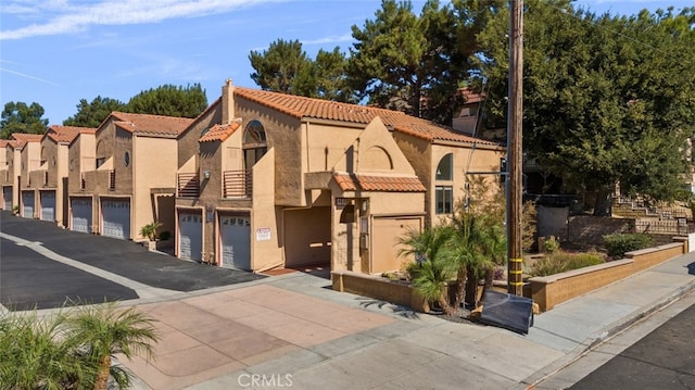 view of front of home featuring stucco siding, a tiled roof, a residential view, and community garages