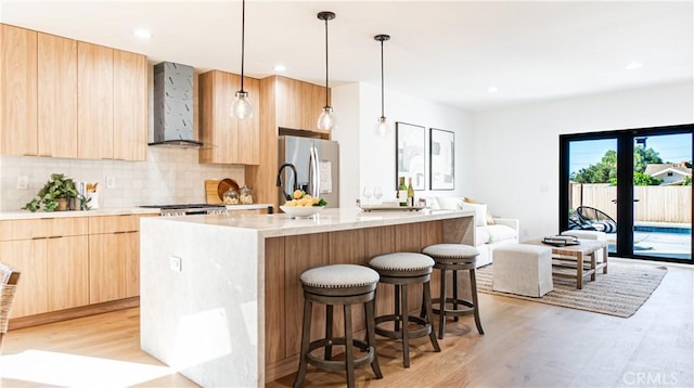 6652 Hough St, Los Angeles, CA 90042 - kitchen featuring stainless steel fridge, modern cabinets, wall chimney range hood, a kitchen bar, and light brown cabinetry