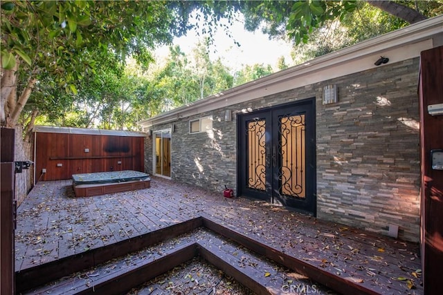 exterior space featuring a jacuzzi, fence, stone siding, french doors, and a wooden deck