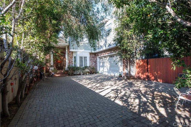 view of front of house with brick siding, decorative driveway, and fence