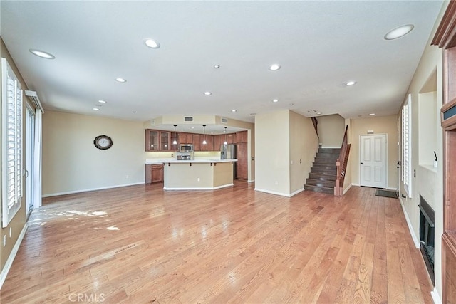 unfurnished living room featuring a fireplace, recessed lighting, light wood-style floors, baseboards, and stairs