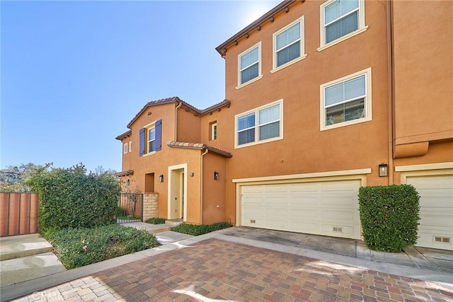 townhome / multi-family property featuring a garage, decorative driveway, fence, and stucco siding