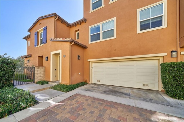 multi unit property with a garage, a tiled roof, fence, decorative driveway, and stucco siding