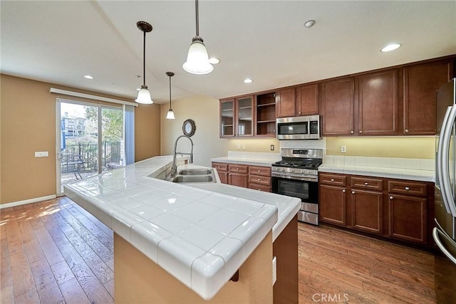 kitchen featuring stainless steel appliances, tile counters, a sink, and wood finished floors