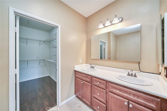 bathroom with double vanity, a spacious closet, baseboards, and a sink