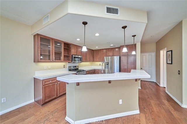 kitchen featuring stainless steel appliances, brown cabinetry, visible vents, and light wood-style floors