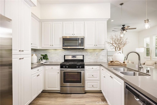 kitchen featuring stainless steel appliances, a sink, white cabinets, light wood-type flooring, and backsplash