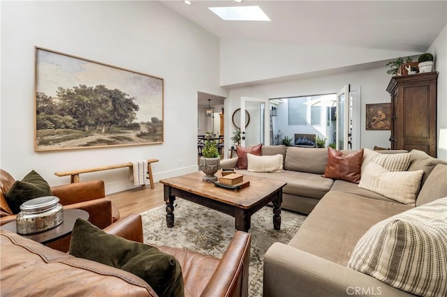 living area featuring high vaulted ceiling, a skylight, light wood-style flooring, and baseboards