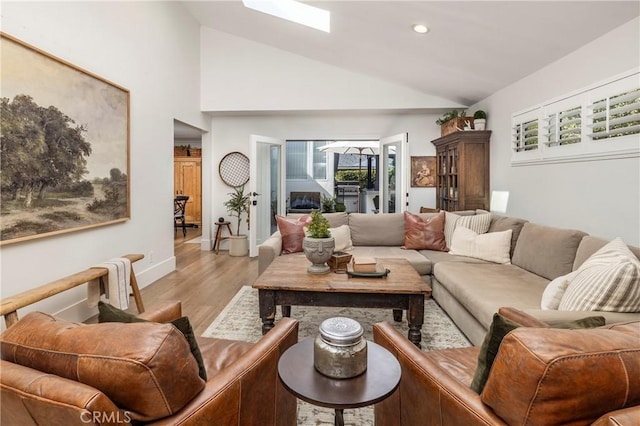 living area featuring a skylight, recessed lighting, high vaulted ceiling, light wood-type flooring, and baseboards