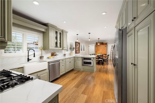 kitchen featuring backsplash, light wood-style flooring, appliances with stainless steel finishes, glass insert cabinets, and a peninsula