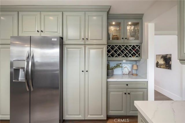 bar featuring dark wood-type flooring, a dry bar, baseboards, stainless steel fridge with ice dispenser, and tasteful backsplash