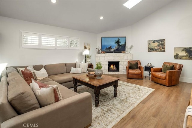 living area with high vaulted ceiling, a stone fireplace, recessed lighting, a skylight, and light wood-style floors