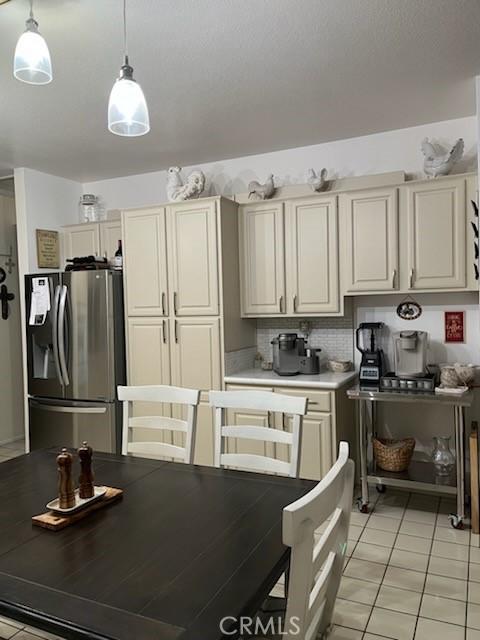 kitchen with stainless steel fridge, light countertops, pendant lighting, backsplash, and light tile patterned flooring