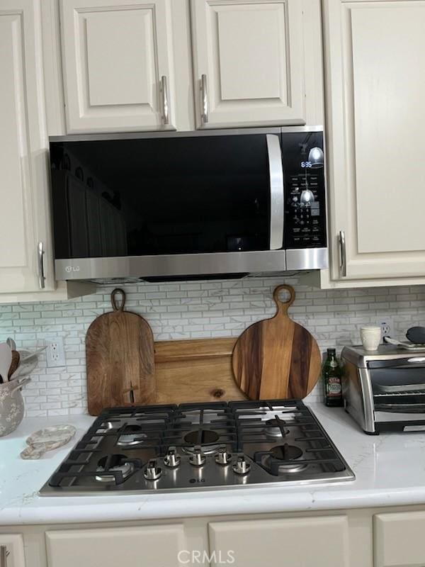 interior details with light countertops, appliances with stainless steel finishes, white cabinetry, and tasteful backsplash