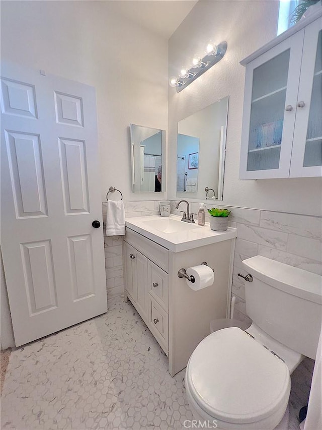 bathroom featuring toilet, wainscoting, vanity, and tile walls