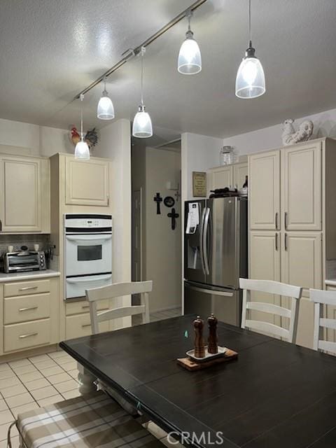 kitchen with oven, light countertops, cream cabinetry, stainless steel refrigerator with ice dispenser, and a warming drawer