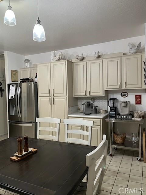 kitchen featuring stainless steel refrigerator with ice dispenser, light tile patterned floors, light countertops, hanging light fixtures, and decorative backsplash